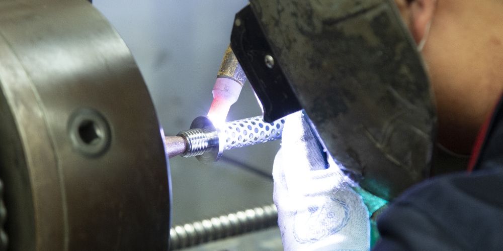 The welding operator is welding the end cap and perforated tube together.